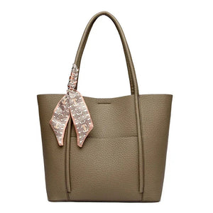Brown tote bag with a pink patterned scarf draped over the handle on a white background
