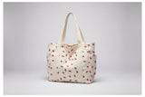 Beige tote bag with red floral pattern on a surface near a window.