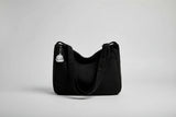 Black corduroy handbag with a keychain on a white surface near a window with blinds.