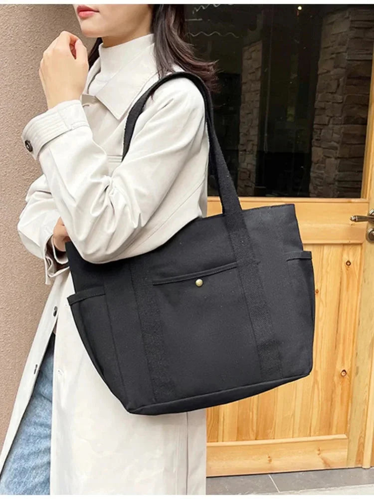 Person holding a black tote bag in front of a wooden door.