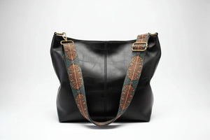 Brown leather handbag with decorative strap on a white background