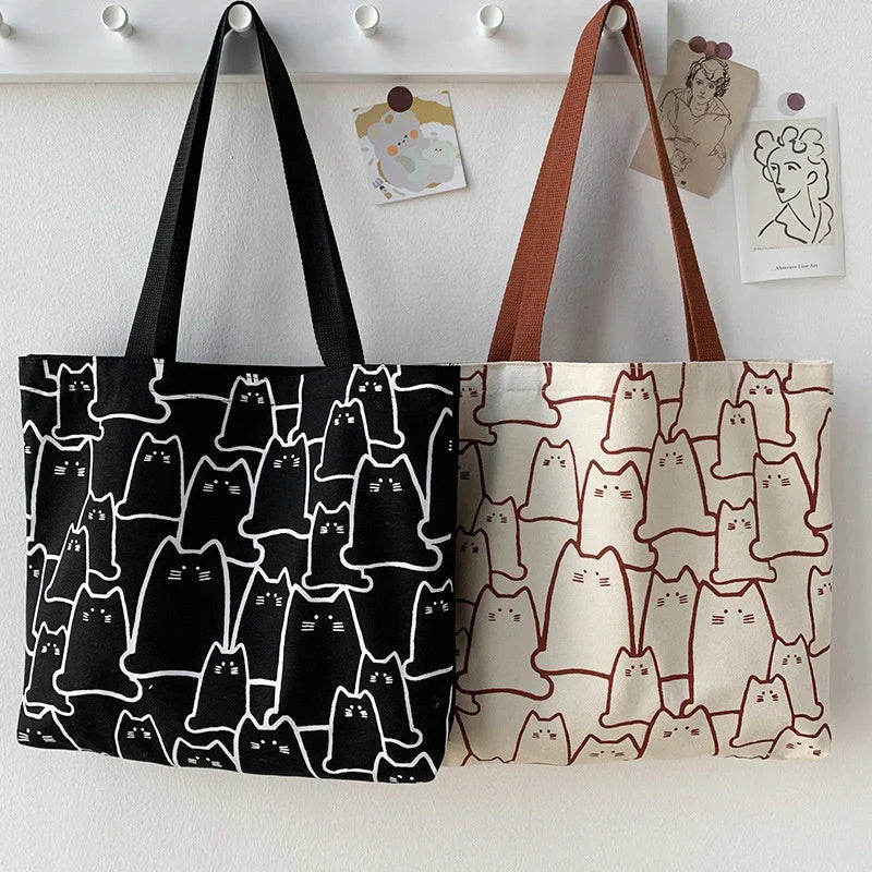Two tote bags with cat patterns hanging on a white wall.