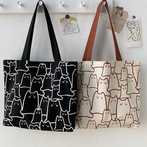 Two tote bags with cat patterns hanging on a white wall.