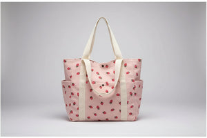 Beige tote bag with red floral pattern on a surface near a window.