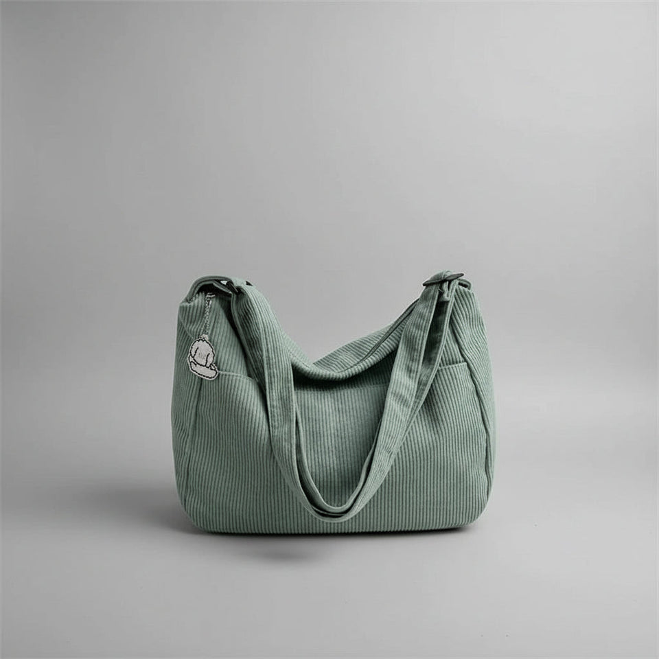 Green corduroy handbag on a white surface with blinds in the background