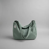 Green corduroy handbag on a white surface with blinds in the background