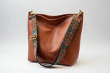 Brown leather handbag with decorative strap on a white background