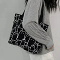 Person holding a black tote bag with white cat patterns against a gray background