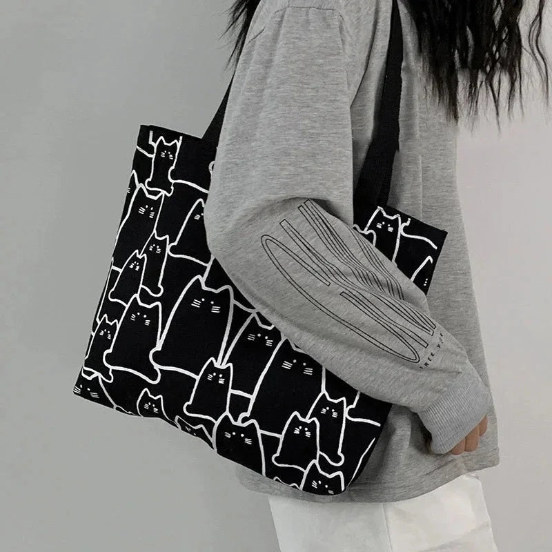 Person holding a black tote bag with white cat patterns against a gray background