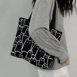 Person holding a black tote bag with white cat patterns against a gray background