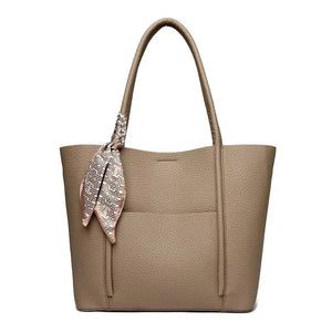 Black leather tote bag with a patterned scarf draped over the handle on a white background