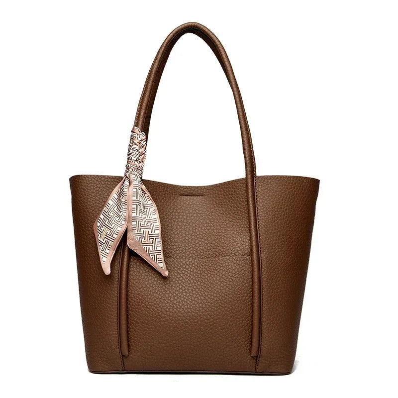 Brown leather tote bag with a decorative scarf on a white background