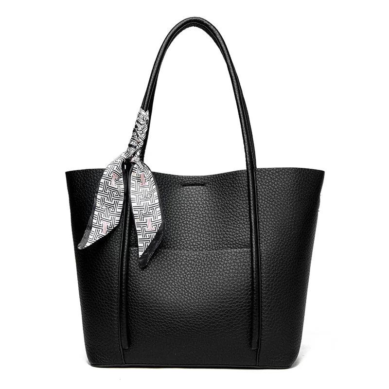 Black leather tote bag with a patterned scarf draped over the handle on a white background