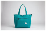 Green jacket and teal bag on a white surface with denim jacket and glass of water.