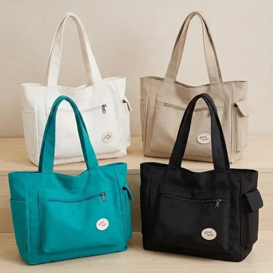 Four handbags in white, beige, teal, and black on a wooden surface with a neutral background.