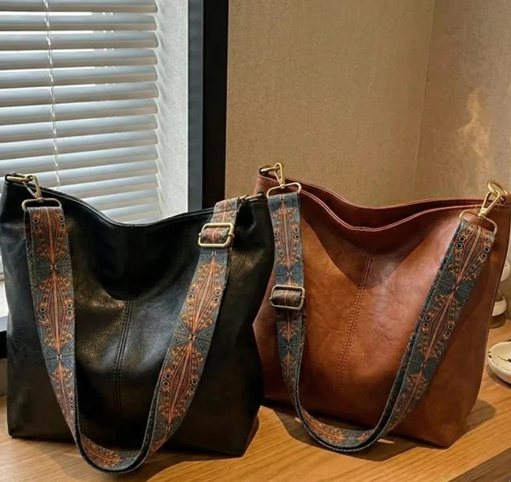 Two leather handbags, one black and one brown, with decorative straps on a wooden surface.