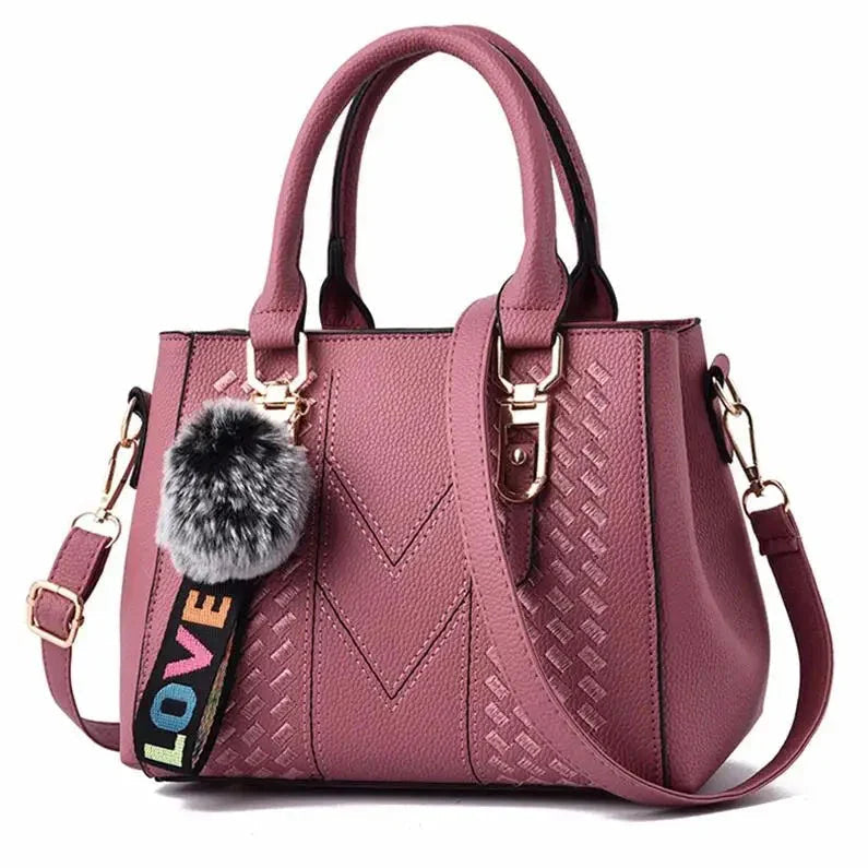 Pink handbag with a decorative strap and pom-pom on a white background