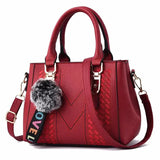 Red handbag with a fur pom-pom and colorful strap on a white background